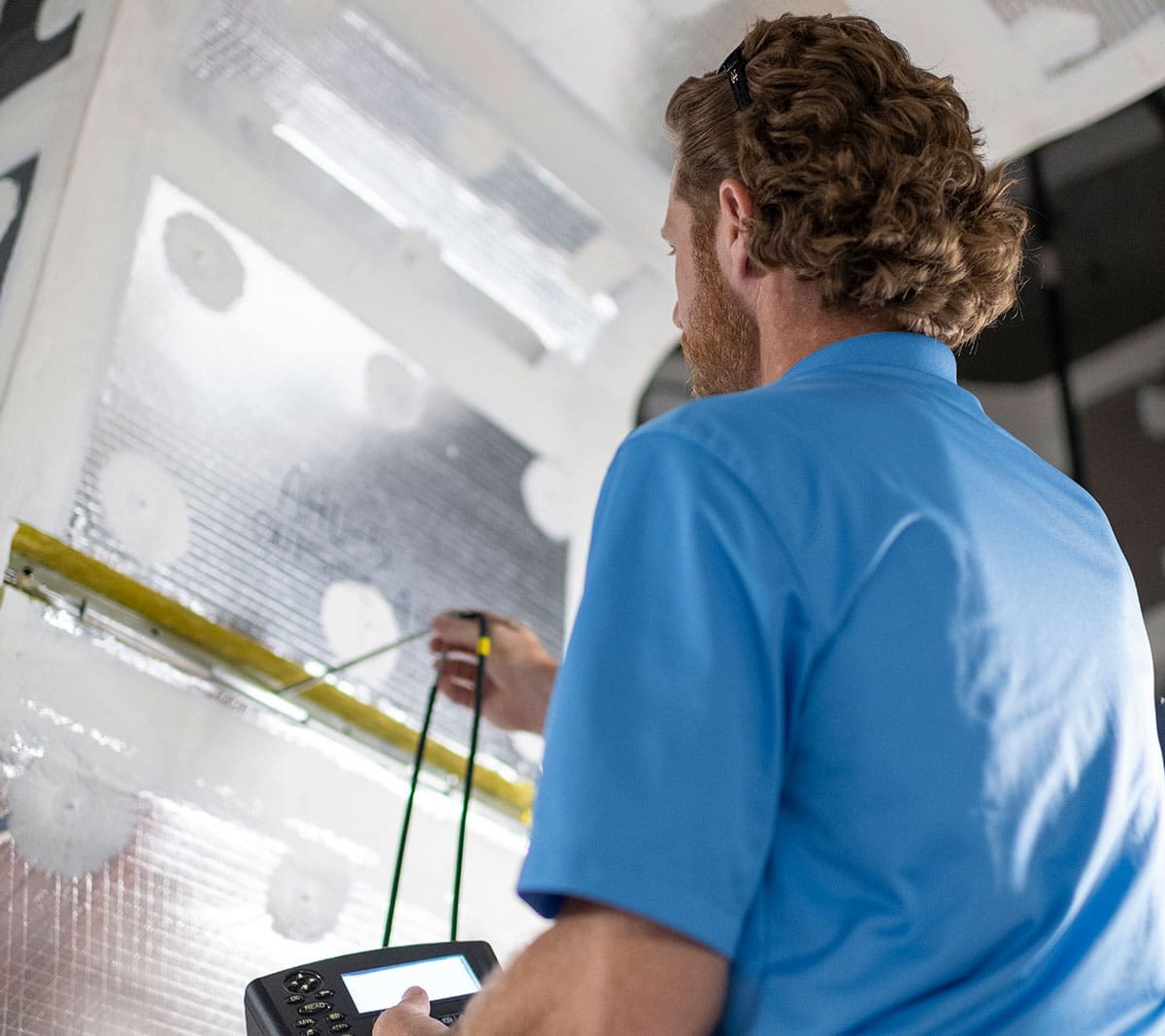 technician-handheld-testing-device-hvac-air-handler-inspection-sita. Technician using a handheld testing device to inspect HVAC equipment