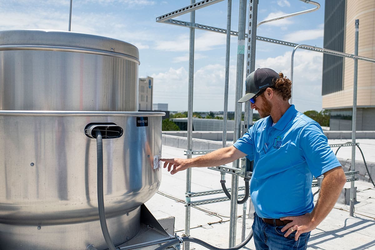 worker-inspecting-commercial-rooftop-ventilation-system-sita Worker examining rooftop stainless steel ventilation equipment on a commercial building.