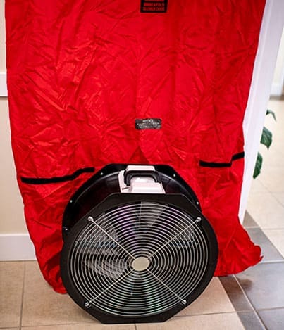 Blower door fan installed in red doorway panel for air leakage testing.