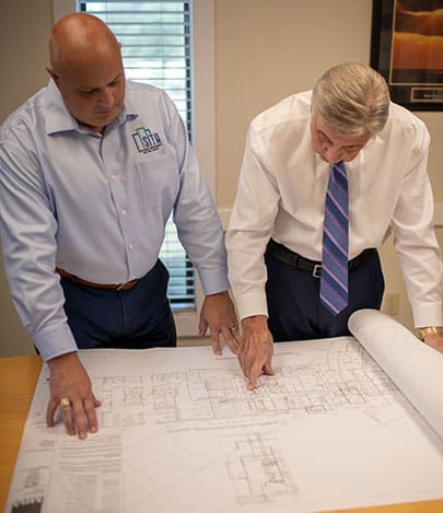 Two engineering professionals reviewing architectural blueprints on a conference table during a project planning meeting.