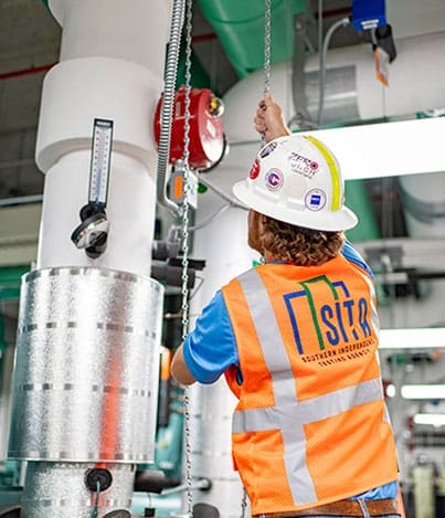 Technician in SITA safety vest adjusting overhead mechanical equipment.