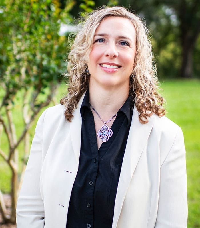 smiling-woman-curly-blonde-hair-white-blazer-outdoor-headshot-sita. A headshot of Donna Peachy, Director of Operations from SITA smiling and posing outdoors