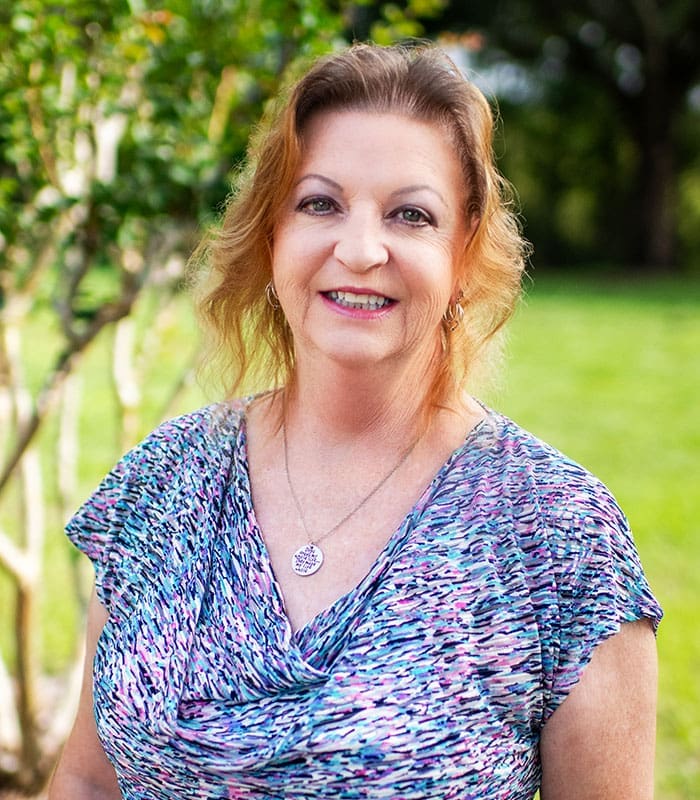 lynn-challandes-project-administrator-headshot-outdoors-sita. Outdoor professional headshot of Lynn Challandes, Project Administrator at SITA, smiling in a garden setting.