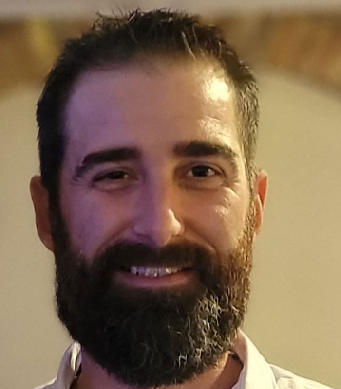 smiling-man-dark-beard-headshot-portrait-sita. A headshot of Tyler Perkins smiling with dark beard and short hair headshot