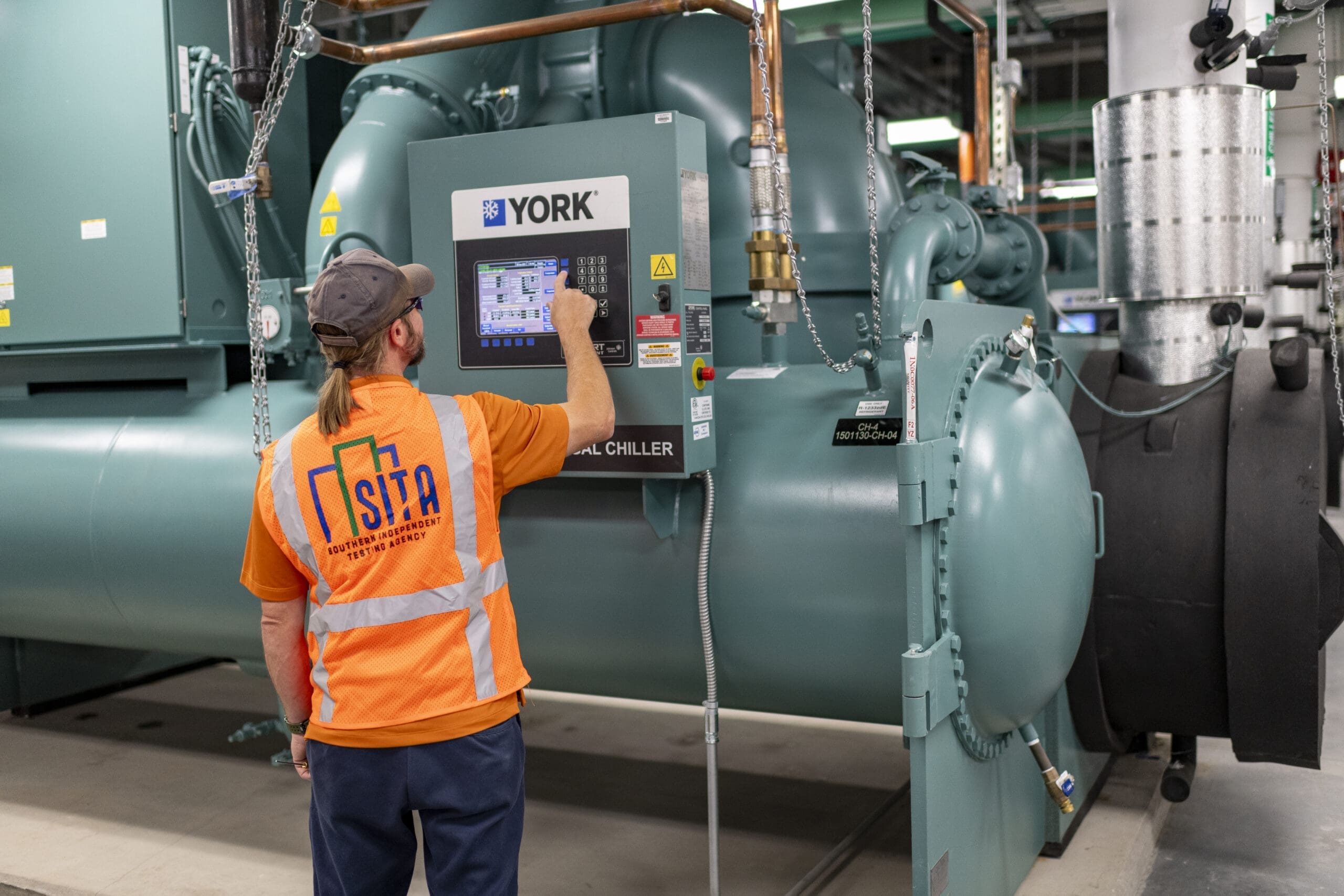 sita-technician-operating-york-chiller-control-panel-commissioning-sita. SITA technician operating a YORK chiller control panel during HVAC commissioning and mechanical system performance testing.