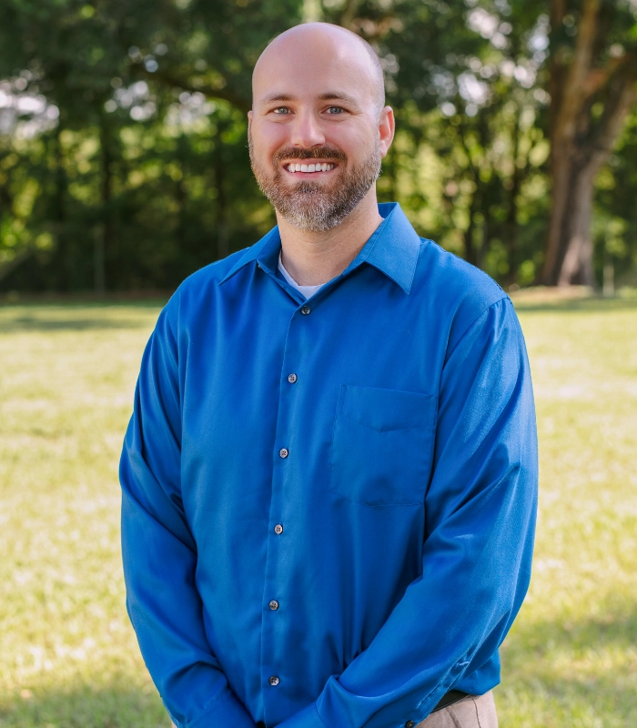 SITA team member in a blue dress shirt smiling outdoors in a shaded green setting