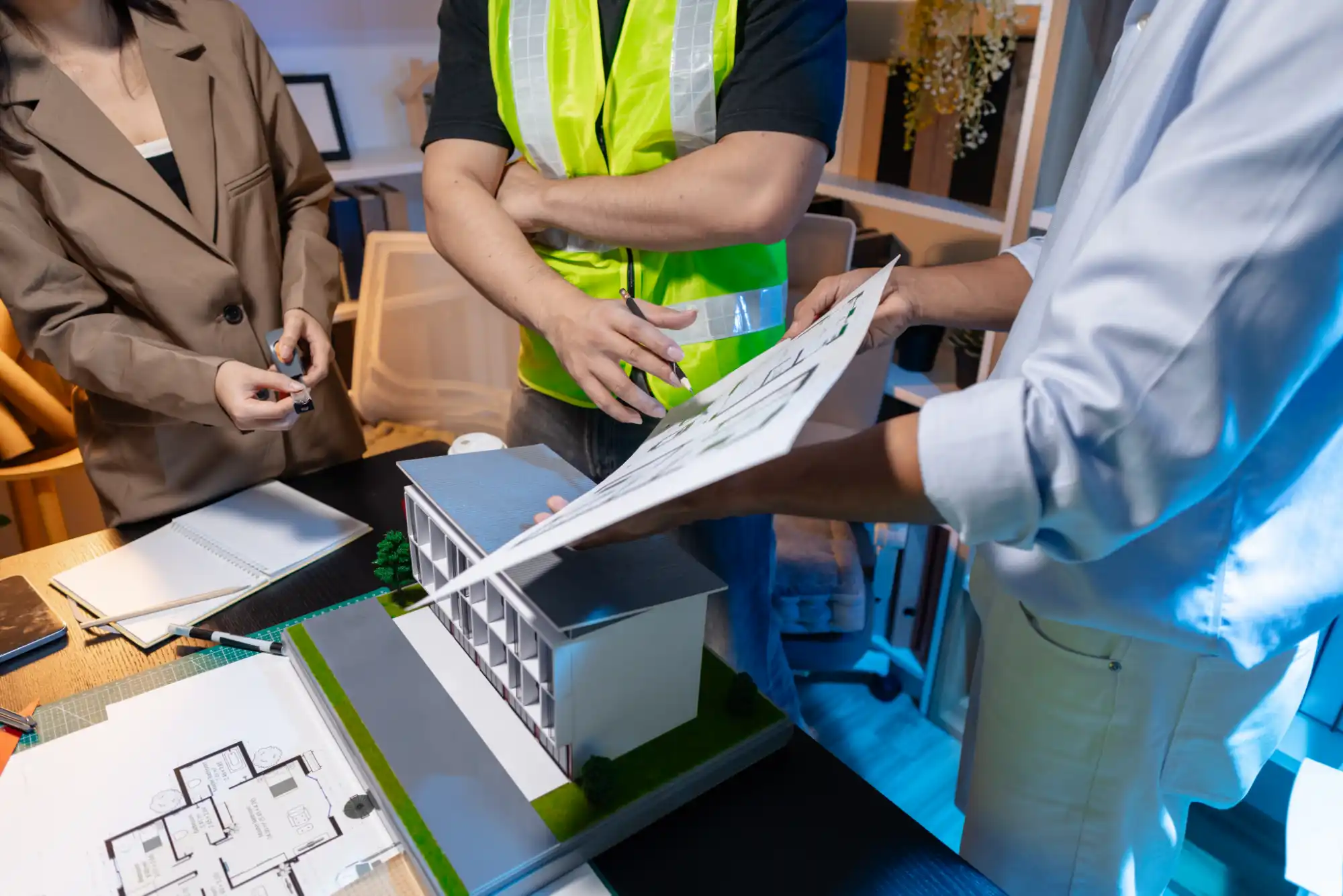 team-reviewing-building-performance-plans-sita. Team of professionals in safety vest and business attire review architectural drawings and a building model during construction planning and verification