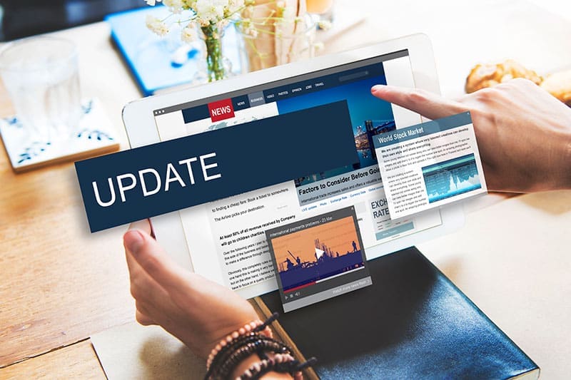 tablet-news-update-digital-content-sita. Person holding a tablet displaying a news website with an "Update" graphic overlay and multiple digital content panels fanning outward