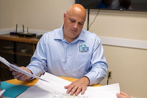 brian-kaupp-reviewing-blueprints-in-office-sita. Brian Kaupp reviewing blueprints at a desk in an office.