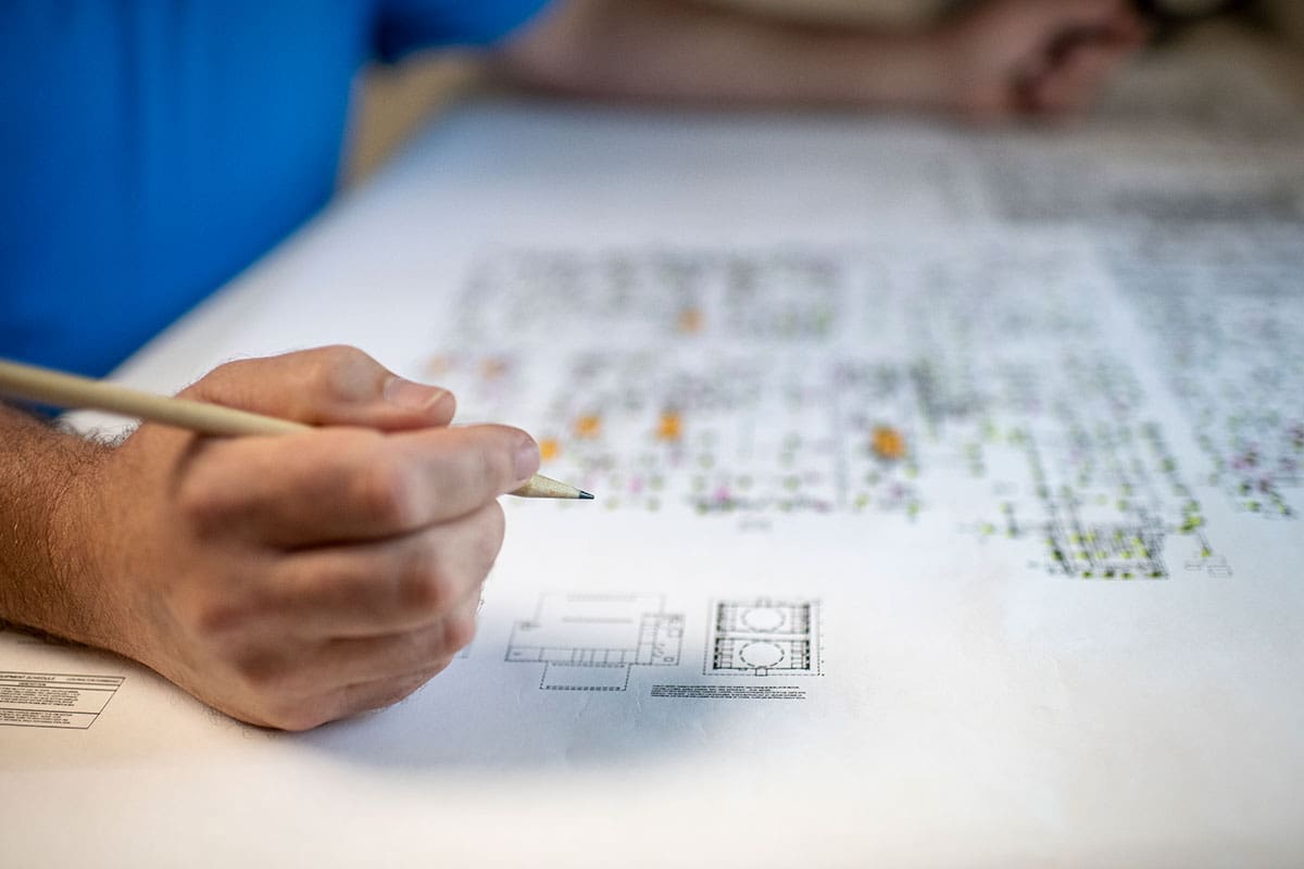 hand-pencil-pointing-colorful-mechanical-blueprints-table-sita. Close-up of a hand holding a pencil over colorful mechanical blueprints on a table