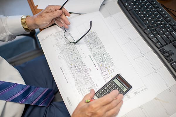 hvac-engineer-reviewing-building-plans-and-system-analysis-sita. Engineer reviewing HVAC building plans with a calculator and technical drawings during project analysis and commissioning preparation.