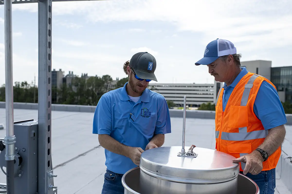 sita-technicians-rooftop-hvac-system-inspection-sita. Two SITA technicians inspecting and installing rooftop HVAC testing equipment during a commercial building performance assessment.