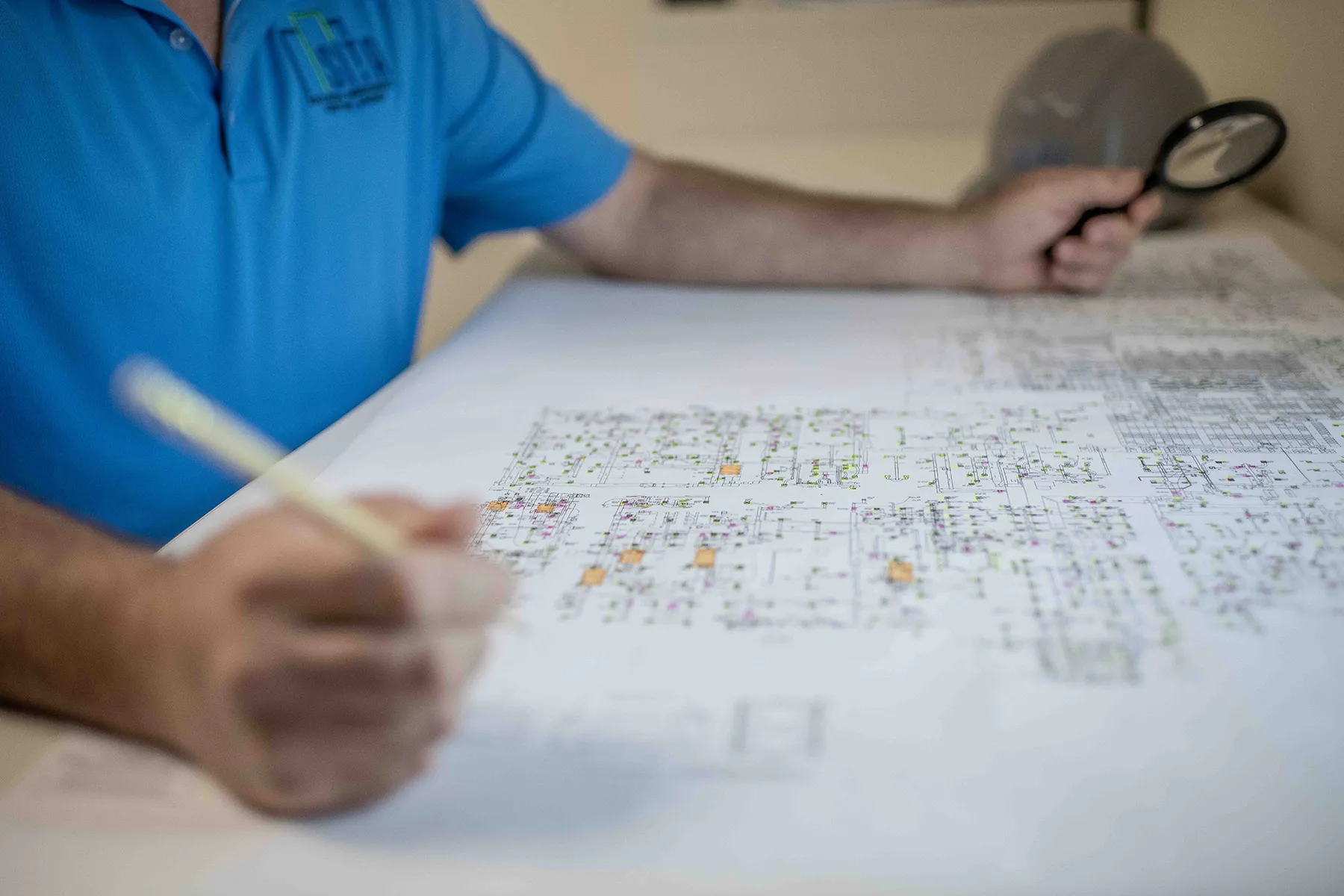 engineer-reviewing-hvac-commissioning-plans-for-energy-efficiency-sita. Engineer reviewing detailed HVAC commissioning plans and schematics with a magnifying glass during a system design evaluation.