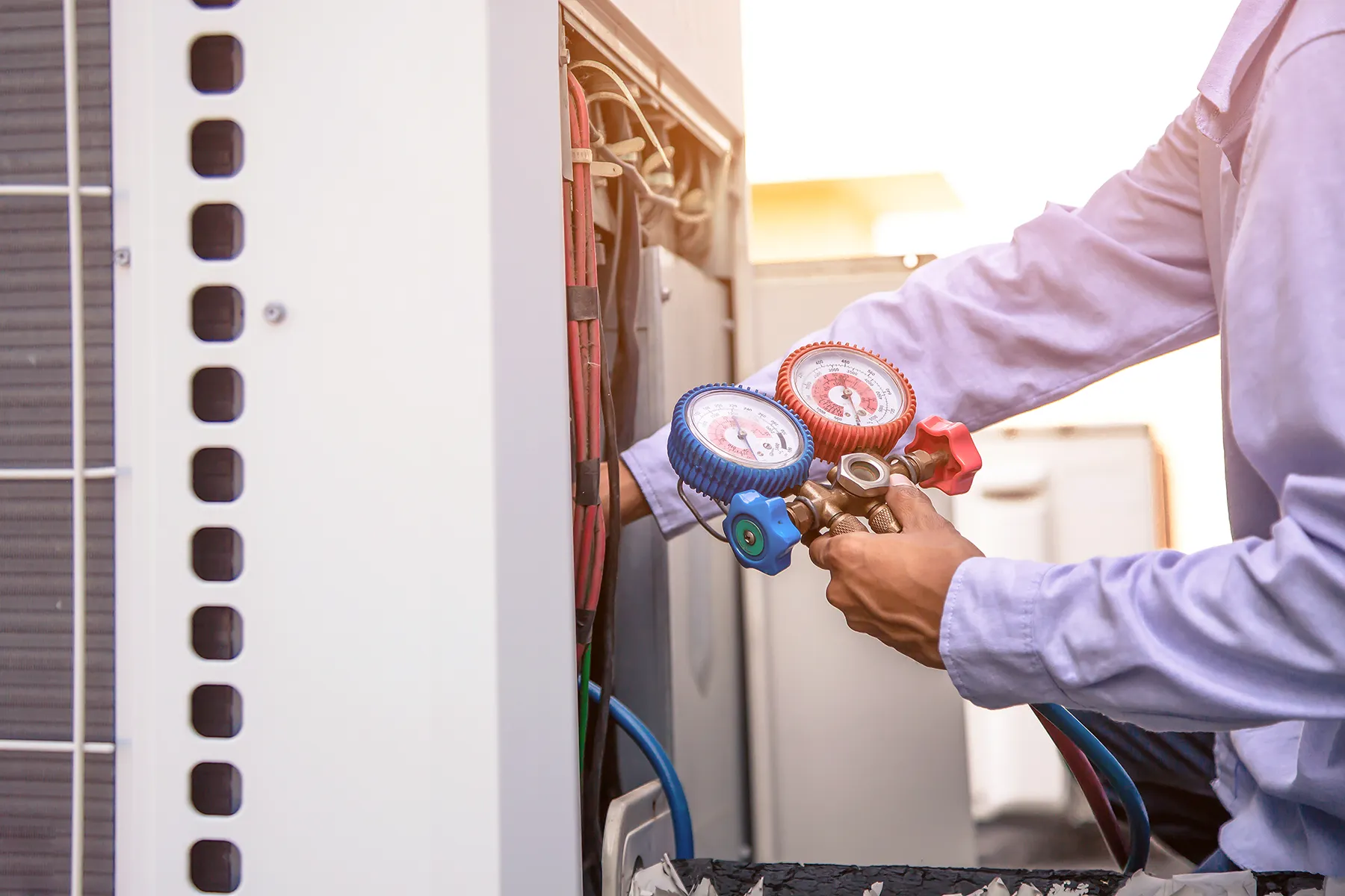 hvac-technician-checking-air-conditioning-pressure-sita. HVAC technician using pressure gauges while servicing and checking refrigerant levels on an outdoor air conditioning unit.