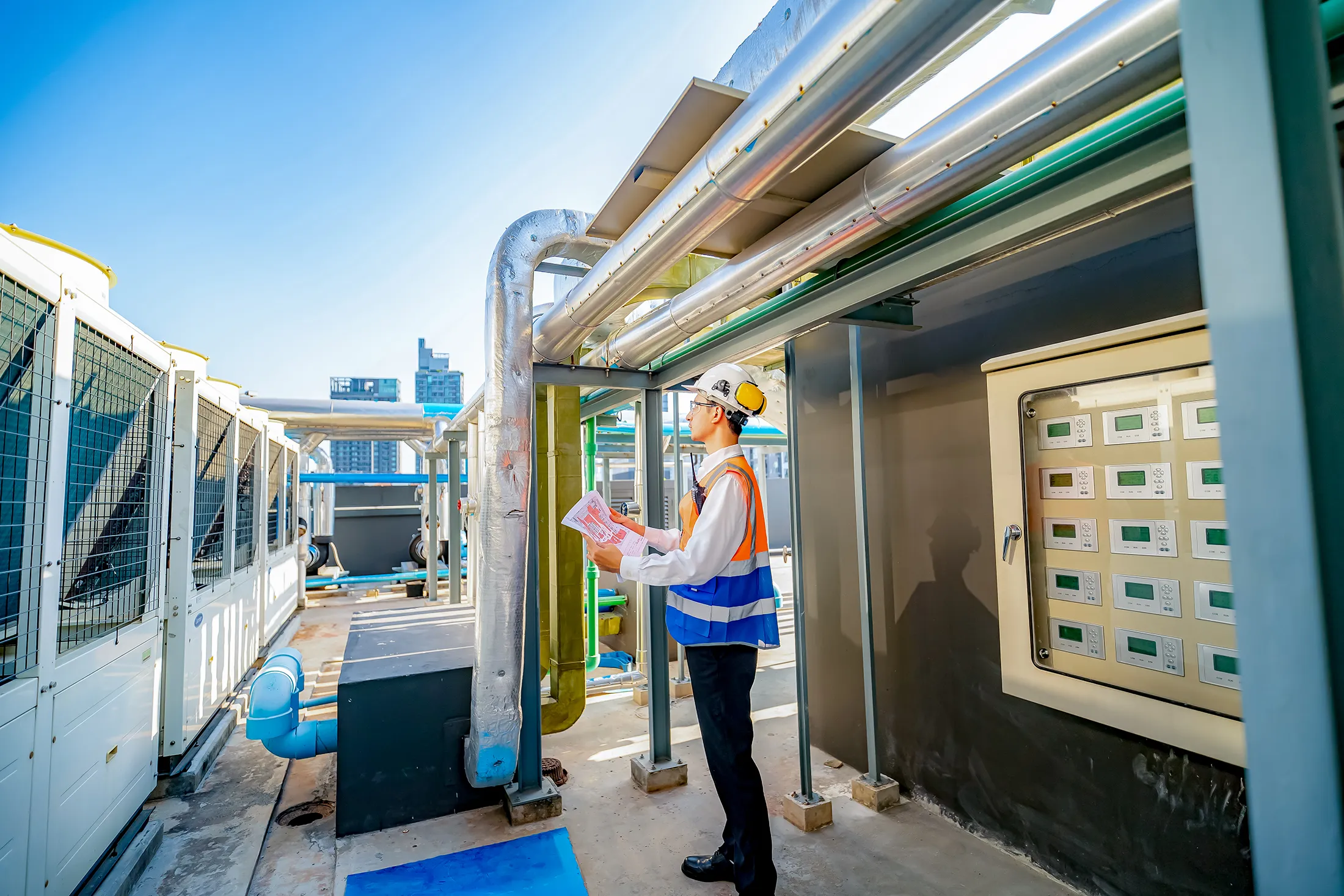 engineer-inspecting-commercial-hvac-and-piping-systems-sita. Engineer inspecting industrial HVAC and ventilation systems on a commercial rooftop with exposed piping and control panels.