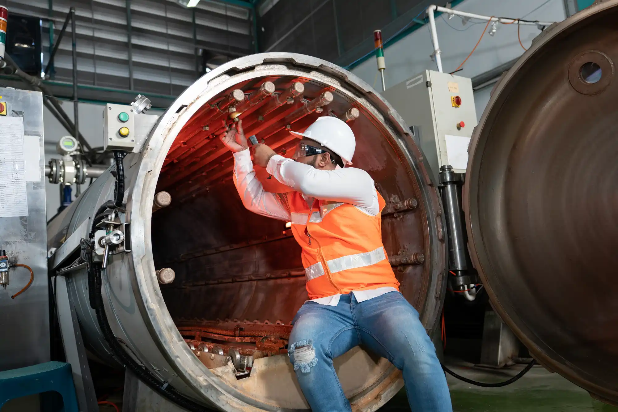 hvac-technician-performing-ductwork-inspection-sita. HVAC technician performing internal inspection and testing inside large red industrial ductwork or air handling unit with measurement equipment and safety gear.