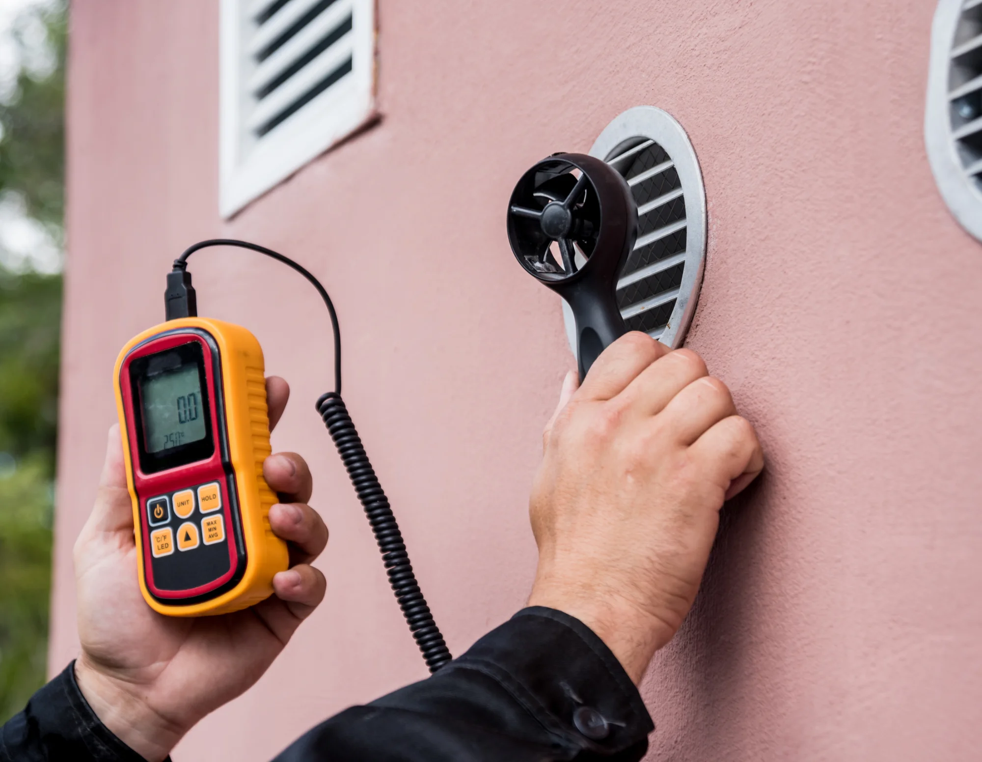 technician-anemometer-measuring-airflow-exterior-wall-vent-sita. Technician using an anemometer to measure airflow at an exterior wall vent